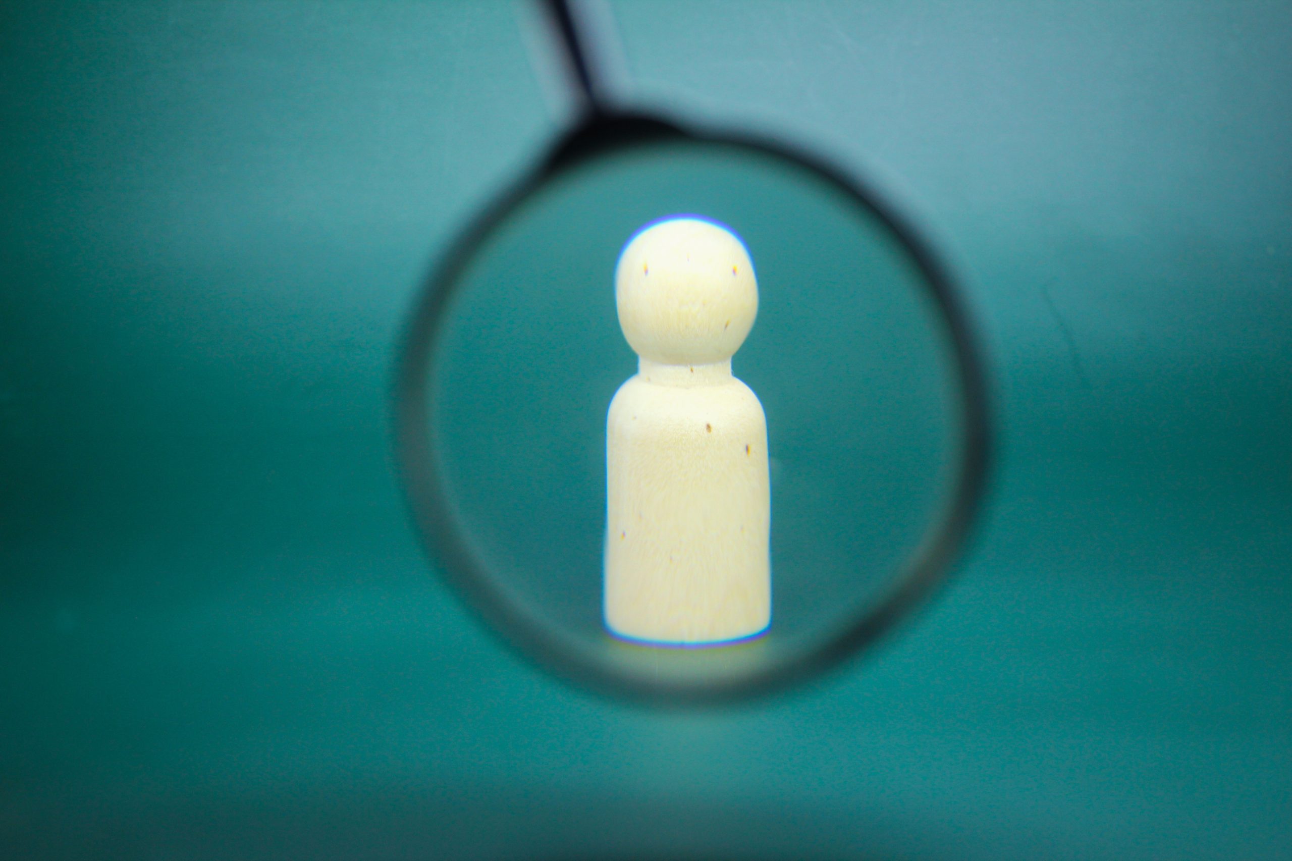 magnifying glass looking at a wooden figure, resembling the close knit effort it takes to spot the early stages of relapse