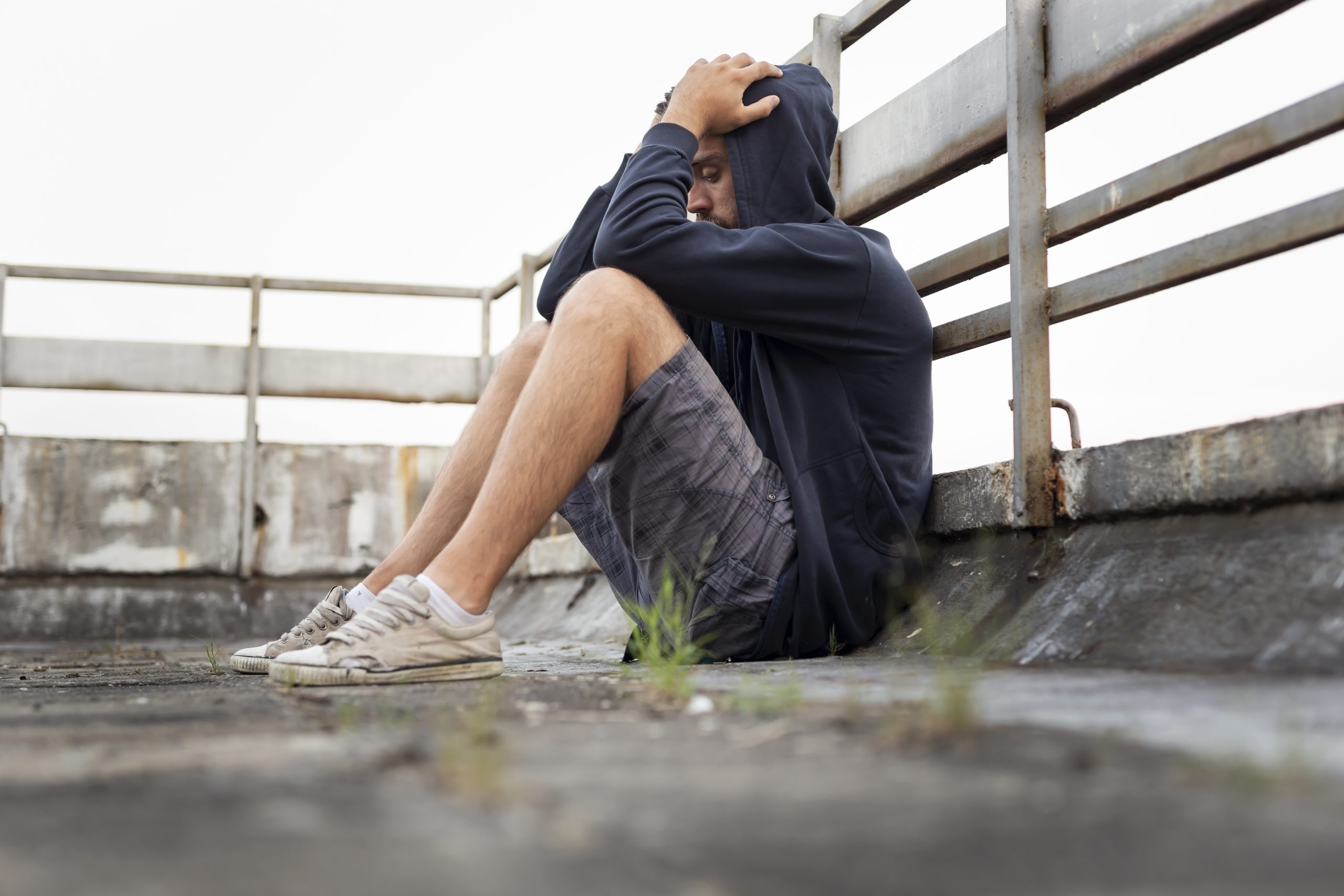 a young man sitting on a pier with his hands on his head, highlighting the devastating link between drugs and depression