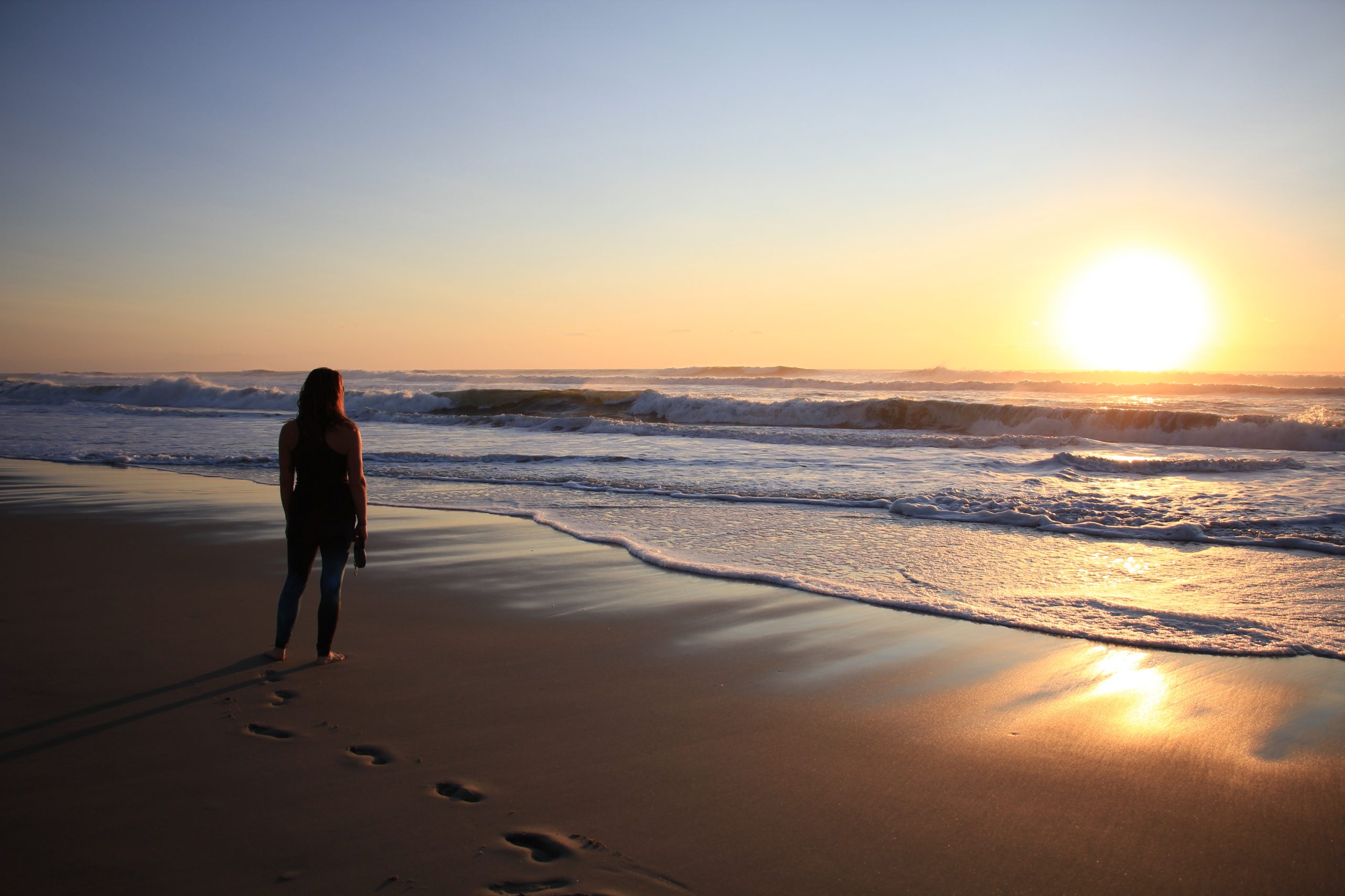 a woman on the beach at sunrise, symbolizing the importance of whole person care