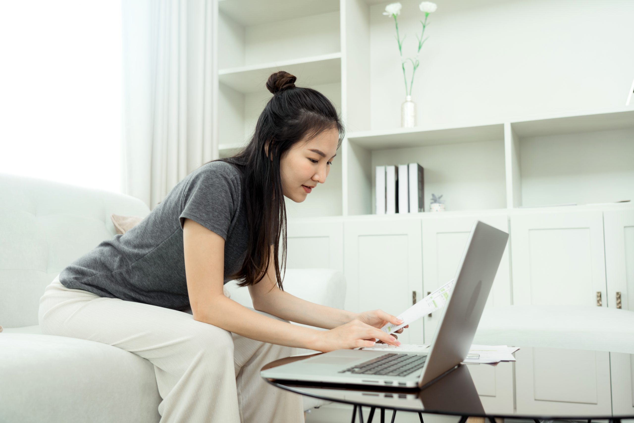 a woman sitting in her living room using a calculator and her laptop on money management for recovering addicts