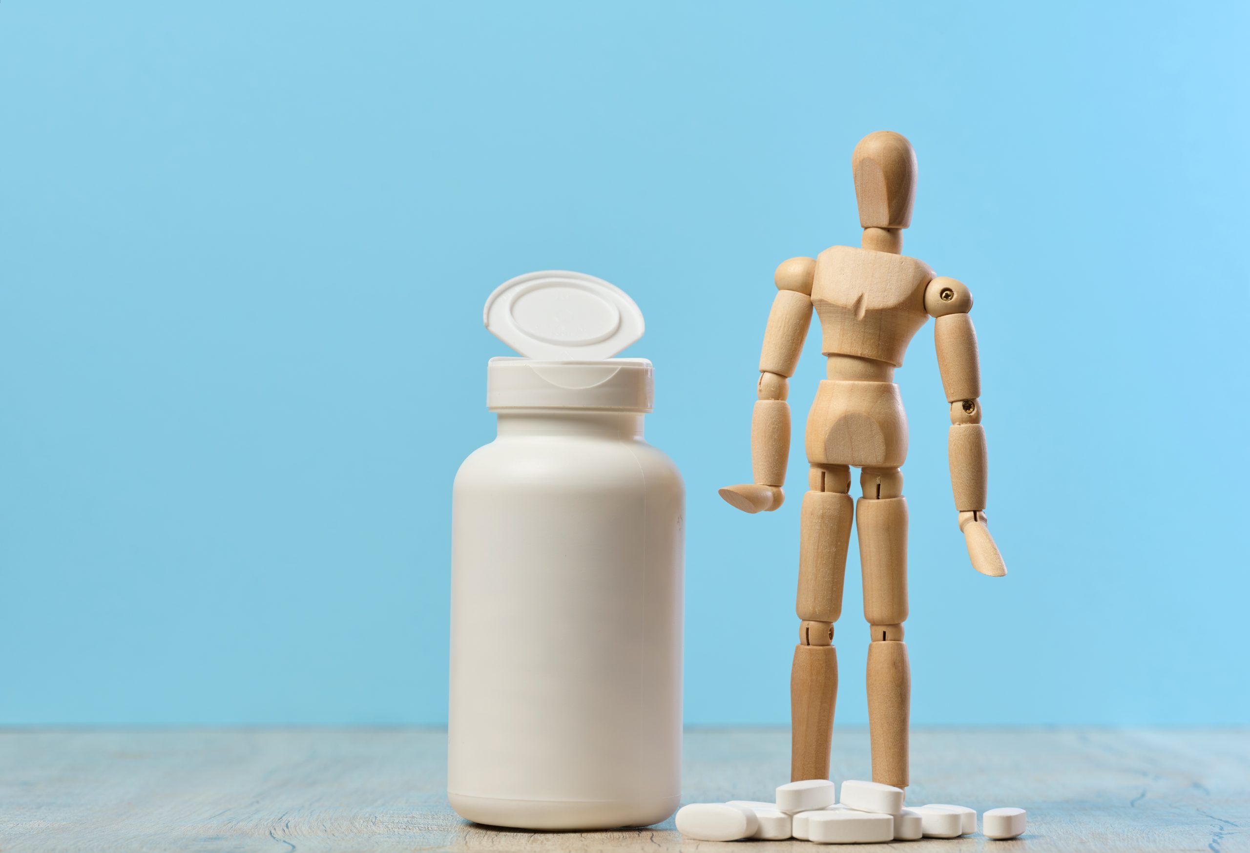 a woody dummy with a plastic bottle and oval white pills on a table, highlighting the withdrawal symptoms of gabapentin