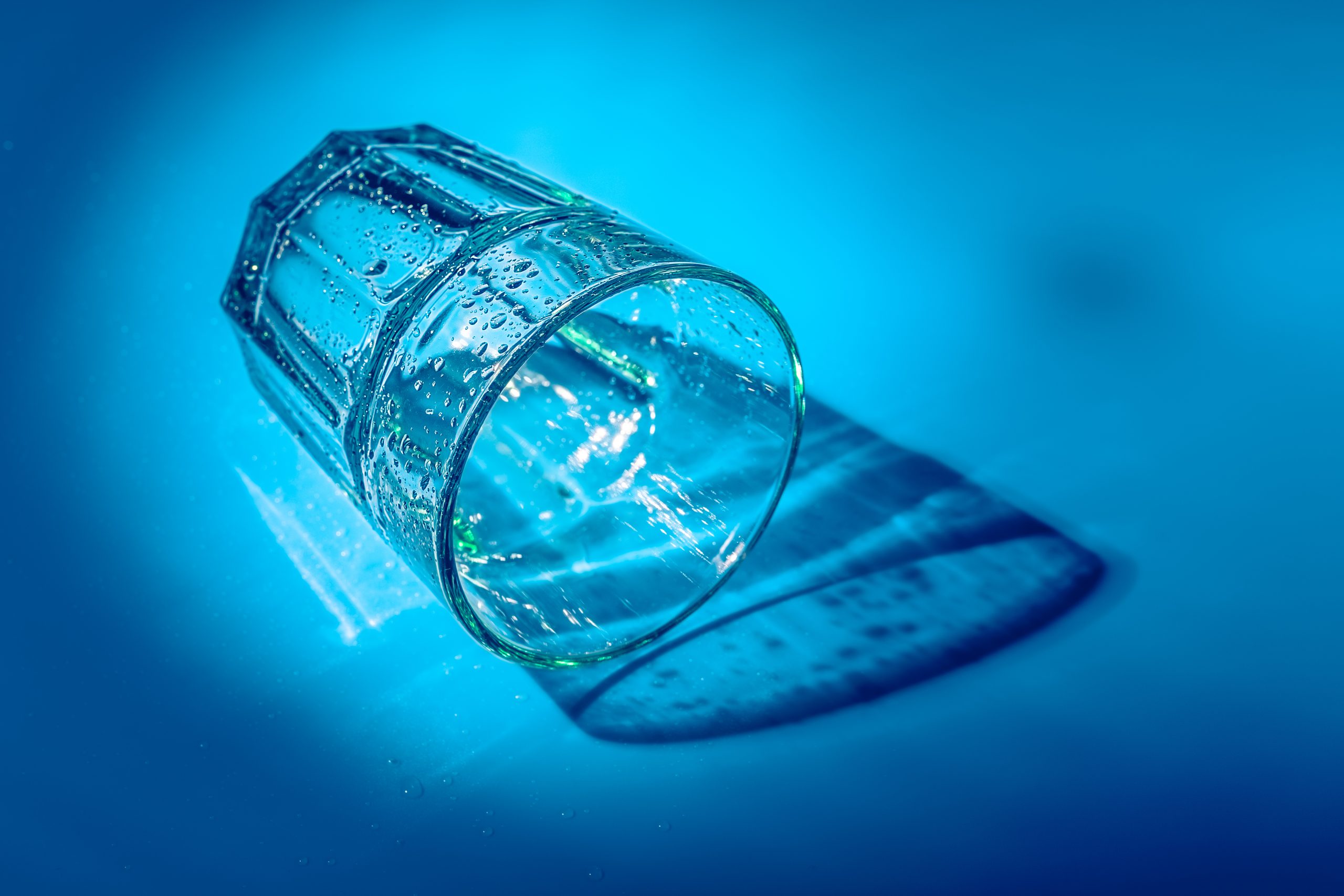 a empty drinking glass on its side against a blue background, symbolizing the riskiness of white knuckle sobriety