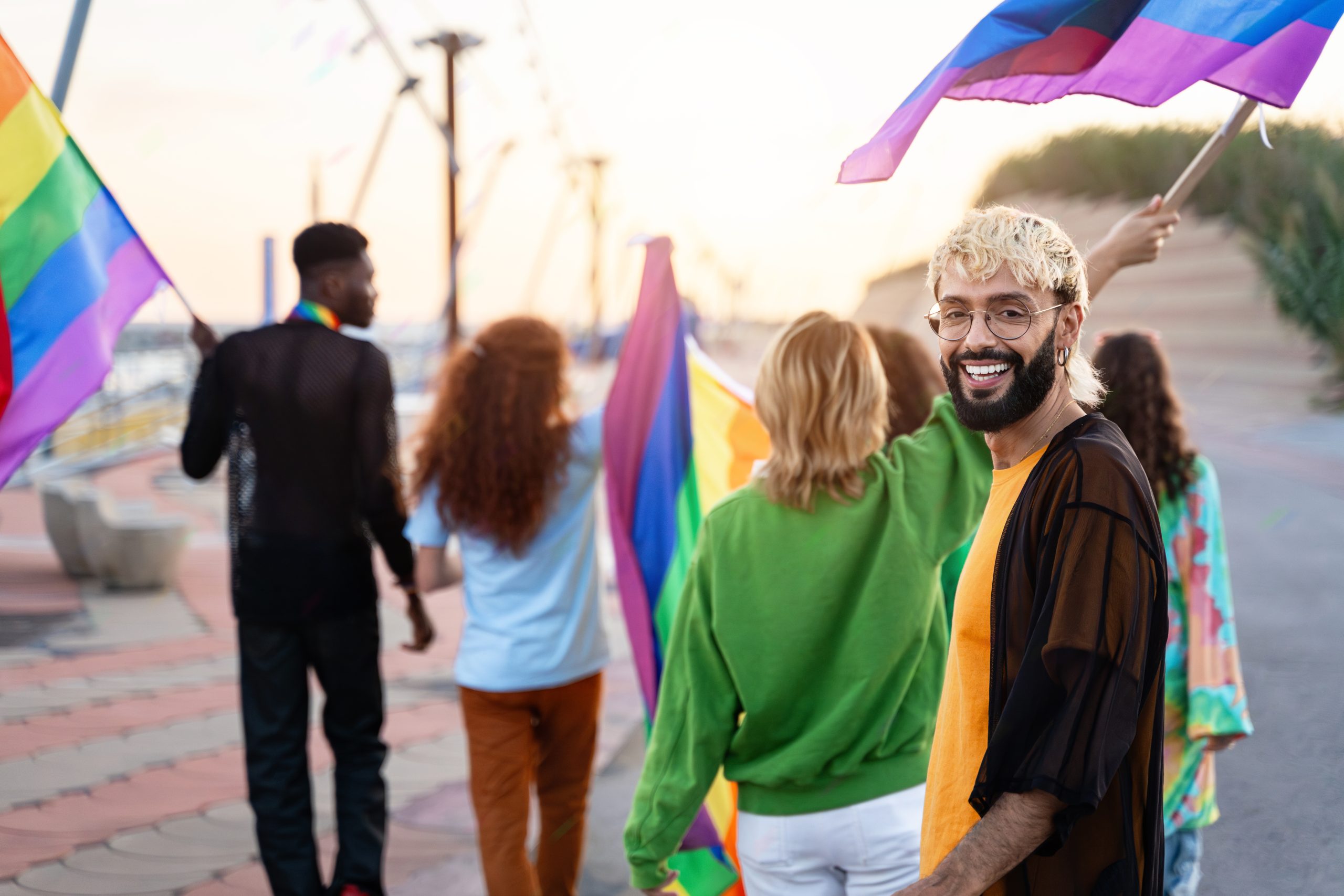 a smiling man with others holding Pride flags in the background, highlighting the importance of LGBTQ addiction treatment