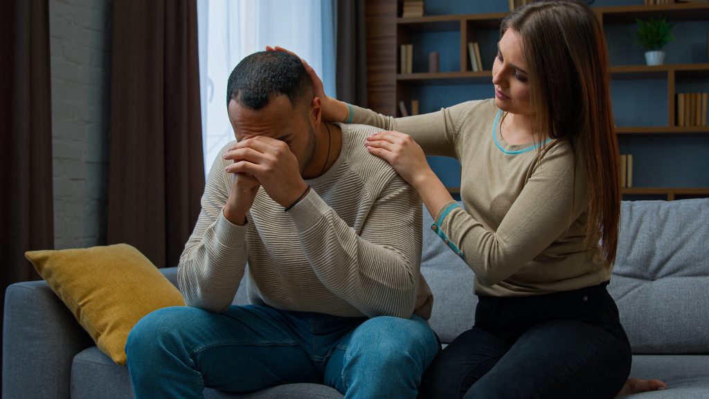 a woman consoling a man on the couch as part of living with an addict