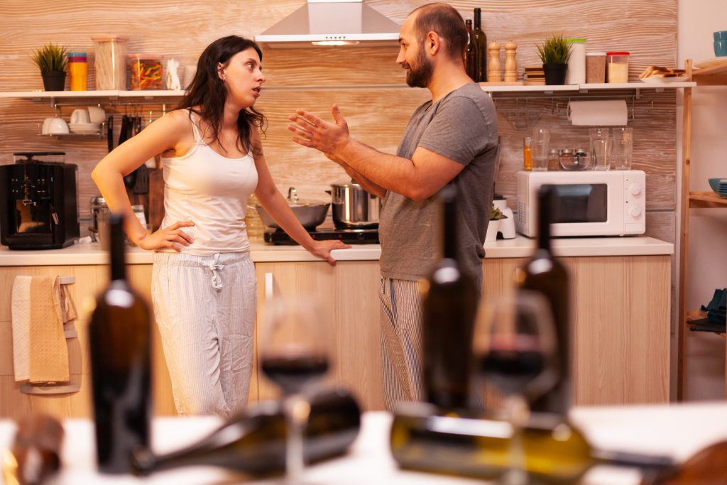 a man and woman arguing in the kitchen surrounded by alcohol glasses to show when to leave an alcoholic