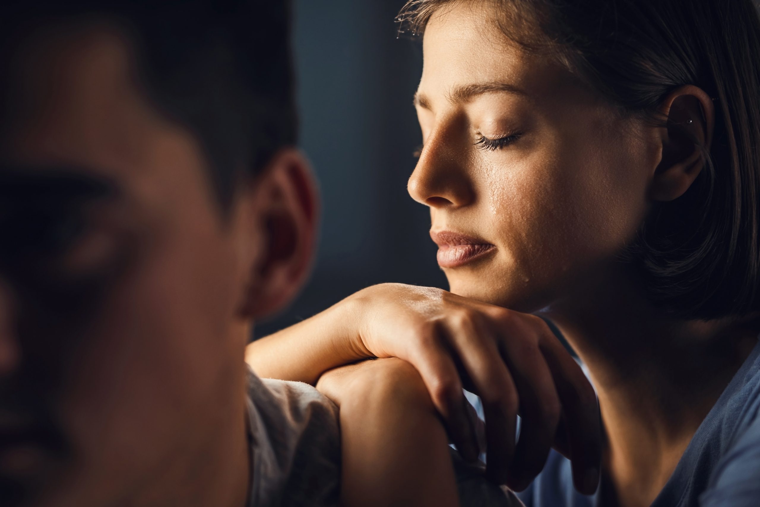 Sad woman crying with eyes closed while leaning on boyfriend's shoulder.