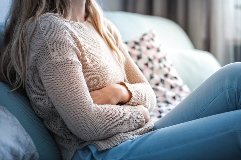 woman sitting on couch holding her stomach to show the link between ulcers and alcohol