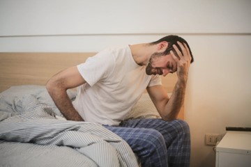 a man sitting on the edge of his bed after finding blood in stool after drinking alcohol