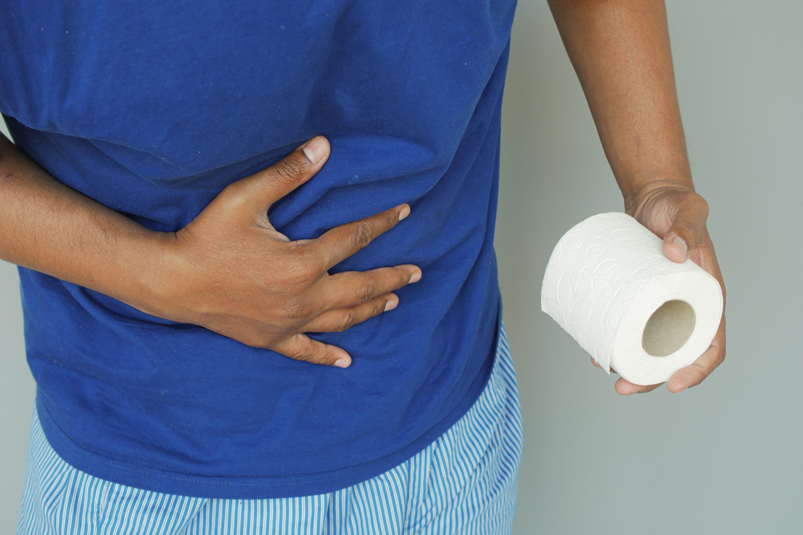 man gripping his stomach while holding toilet paper to represent black stool after drinking