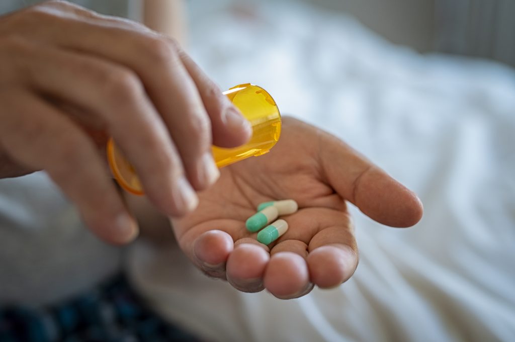 a man pouring pills from a bottle into his hand as he believes prozac for alcoholism is a treatment