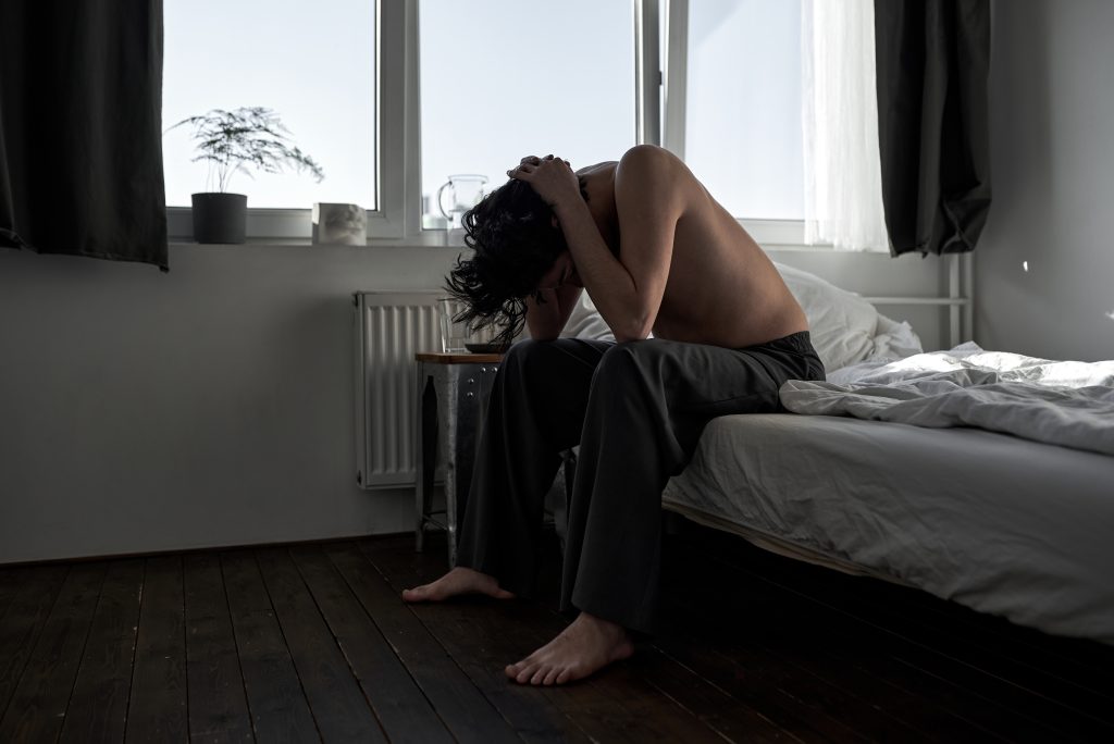 young man sitting on the edge of his bed suffering from withdrawal symptoms of doxepin